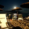 Spiaggia notturna con luna piena e ombrelloni.
