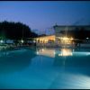 Piscina illuminata di sera con sedie a sdraio attorno e un edificio sullo sfondo.