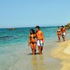 Coppia cammina sul bagnasciuga, mare limpido.