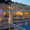 Piscina illuminata di sera, con lettini e edificio sullo sfondo.