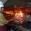 Cuoco che griglia davanti a un fuoco vivo.