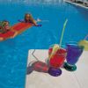 Due persone su materassini in piscina, bevande colorate con cannucce sul bordo.