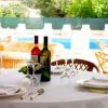 Tavolo apparecchiato con vino e bicchieri, vista su piscina e sedie in vimini.