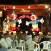 Uno spettacolo con clown gonfiabili giganti e pubblico seduto su sedie di plastica bianca.