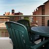 Balcone con tavolo e sedie verdi, vista su tetti di edifici e cielo azzurro.