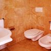 Bagno rivestito in piastrelle beige con lavabo, WC e bidet.