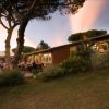 Persone sedute all'aperto vicino a un edificio in un giardino con alberi e cespugli al tramonto.