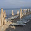 Spiaggia con lettini e ombrelloni chiusi allineati sulla sabbia, vista mare.