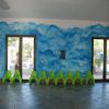 Sala con muri blu, sedie verdi e porte-finestre.