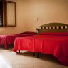 Due letti con coperte rosse in una camera semplice con pareti beige.