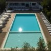 Piscina rettangolare circondata da lettini e ombrelloni bianchi.
