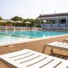 Piscina con bordo in legno, affiancata da lettini e una struttura bianca sullo sfondo.