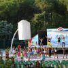 Persone fanno esercizi su un palco all'aperto, circondate da sedie e alberi.