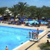 Piscina all'aperto con ombrelloni blu e palme intorno. Persone sulla piattaforma e sdraio.