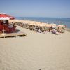 Spiaggia sabbiosa con lettini, ombrelloni arancioni e chiosco rosso.