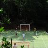 Persone giocano a calcio in un campo all'aperto circondato da alberi.