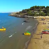 Spiaggia sabbiosa con ombrelloni colorati e pedalò gialli in mare.