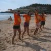 Gruppo di persone sulla spiaggia, indossano magliette arancioni.