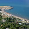 Spiaggia affollata con file di ombrelloni colorati e un mare blu limpido.