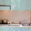 Piccola cucina con pensili azzurri, fornello con pentole e lavello.