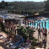 Piscina all'aperto con persone che fanno esercizi, lettini e ombrelloni.