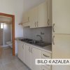 Cucina compatta con mobili chiari, lavello e piano cottura. In fondo, una porta verso il bagno.