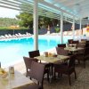 Piscina con sedie a sdraio e tavoli all'aperto sotto una tettoia bianca.