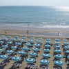 Spiaggia con file di ombrelloni blu e lettini di fronte al mare calmo.