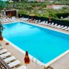 Piscina rettangolare circondata da lettini e ombrelloni colorati.