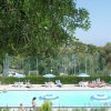 Piscina con ombrelloni, alberi e vista mare.