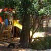 Parco giochi con scivolo giallo tra alberi.