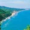 Costa con spiaggia e mare blu, circondata da colline verdi.