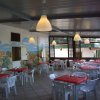 Sala da pranzo interna con tavoli e sedie di plastica bianca.