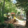 Parco giochi tra alberi con scivolo e altalene.