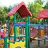 Un parco giochi colorato con casette e ponti per bambini. Alberi verdi intorno.