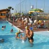 Persone vicino a una piscina con ombrelloni gialli e verdi.