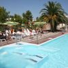Piscina con cascate d’acqua, lettini e ombrelloni gialli e verdi. Palme sullo sfondo.