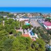Vista aerea di un villaggio turistico con alberi e mare sullo sfondo.