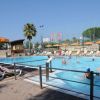 Piscina all'aperto con persone che nuotano, lettini e ombrelloni gialli.