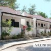 Villette a schiera bianche con piante e vialetto di pietra, immerse tra gli alberi.