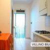 Cucina con tavolo arancione, piano cottura e porta a vetri che lascia entrare la luce.