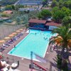 Vista aerea di una piscina con lettini e ombrelloni colorati, circondata da palme e campi sportivi.