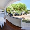 Veranda con tavolo bianco e sedie di plastica, vista su giardino con palme e pini.