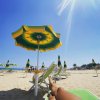 Spiaggia con ombrellone giallo-verde, sedie a sdraio e mare sotto cielo blu soleggiato.