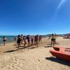 Persone ballano sulla spiaggia vicino al mare sotto un cielo blu.