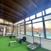 Palestra con tapis roulant, cyclette e rematore su pavimento verde, con grandi finestre.