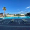 Piscina all'aperto con sdraio, cielo sereno e palme sullo sfondo.