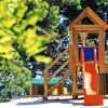 Parco giochi con scivolo arancione e struttura in legno circondato da alberi verdi.