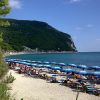Spiaggia con ombrelloni blu, mare e una montagna verde sullo sfondo.