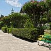 Sentiero con siepi curate e panchina verde tra alberi fioriti.